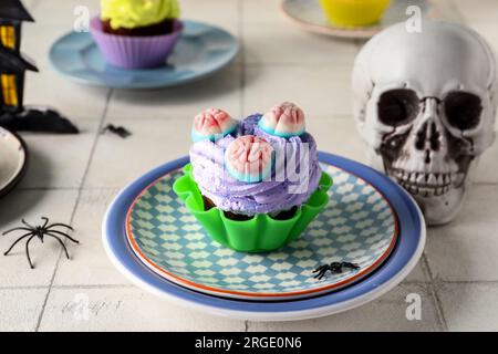 Köstlicher Halloween-Cupcake und Schädel auf hellem Fliesenhintergrund, Nahaufnahme Stockfoto