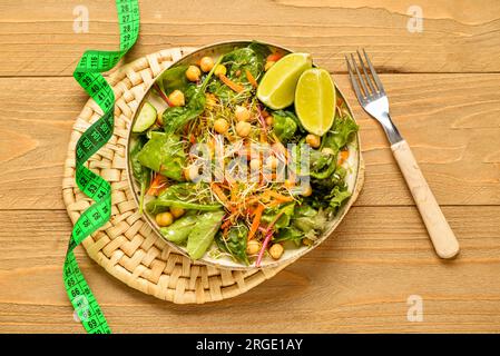 Teller mit frischem Salat und Maßband auf Holzhintergrund. Diätkonzept Stockfoto