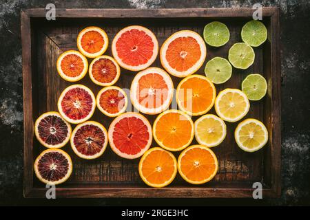 Zitrusfrüchte (Orange, Blutorange, Grapefruit, Zitrone, Limette) in zwei Hälften geschnitten und nach Farbe in einer rustikalen Holzkiste angeordnet Stockfoto