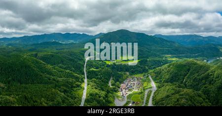Blick aus der Vogelperspektive auf Bergstraßen durch ein kleines Dorf in üppiger grüner Landschaft Stockfoto
