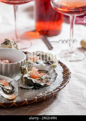 Frische Austern mit rotem Kaviar auf Eis in einer Silberschüssel und Rosenchampagner auf einem weißen Marmortisch Stockfoto