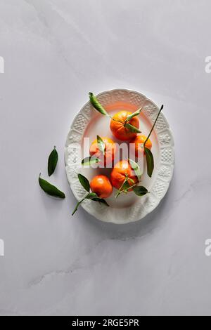 Mandarinenorangen mit Stiel- und Blattdesign auf weißem Teller Stockfoto