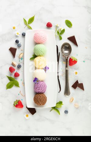 Set aus verschiedenen Eislöffeln und Beeren auf weißem Marmorhintergrund. Erdbeere, Pistazien, Mango, Vanille, Heidelbeere und Schokoladeneis. Oben Stockfoto