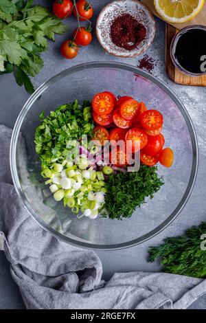 Gehackte Zwiebeln, grüne Zwiebeln, Petersilie, Dill und halbierte Kirschtomaten in einer Glasschüssel. Stockfoto