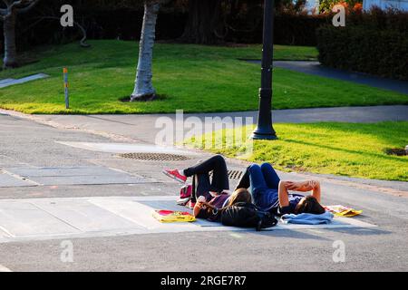 Zwei Studenten liegen auf dem Fußweg auf dem Campus der University of California Berkeley, um den Sonnenuntergang zu beobachten Stockfoto