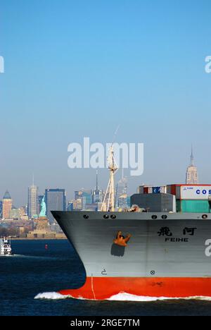 Ein chinesisches Containerschiff fährt durch den Hafen von New York und passiert dabei die Freiheitsstatue, während es Waren und Handel in die USA importiert Stockfoto