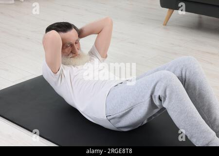 Seniorin in Sportbekleidung, der drinnen auf Fitnessmatte trainiert Stockfoto