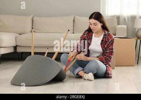 Junge Frau mit Schraubenzieher, die zu Hause einen Sessel auf dem Boden zusammensetzt Stockfoto