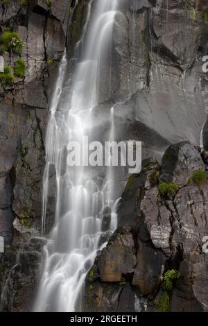 Nahaufnahme eines kleinen Wasserfalls, der eine nasse felsige Klippe hinunterstürzt Stockfoto