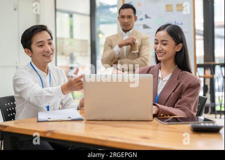 Ein professioneller und glücklicher asiatischer Geschäftsmann teilt seine Ideen mit einer Kollegin in der o, bespricht die Arbeit und plant Pläne für ein neues Projekt Stockfoto