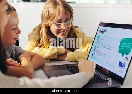 Eine Gruppe junger Kinder lernt, wie ein Code funktioniert, während sie in einem Kurs zur Computerprogrammierung miteinander interagieren. Die Kinder helfen bei der Arbeit Stockfoto