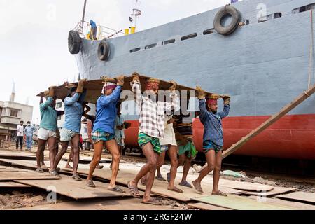 Dhaka, Dhaka, Bangladesch. 9. Aug. 2023. Eine Gruppe von Gepäckträgern trägt eine schwere Stahlplatte von 250 kg auf einer Werft am Ufer des Buriganga in Keraniganj, nahe Dhaka, Bangladesch. Dutzende von Werften, die 30,96 Hektar an der Küste von Buriganga belegen, sind seit 50 Jahren in Betrieb. Es wird hauptsächlich zur Reparatur und Reparatur alter Schiffe und zum Bau neuer Schiffe verwendet. Die Arbeit auf dem Werftplatz funktioniert ohne Helme, Gesichtsmasken oder Sicherheitsschuhe. Sie arbeiten den ganzen Tag lang hart, erhalten aber trotzdem Mindestlöhne. Mit einer zunehmenden Anzahl von Bestellungen sowohl von lokalen als auch von globalen Käufern, ist der Schiffbauer Stockfoto