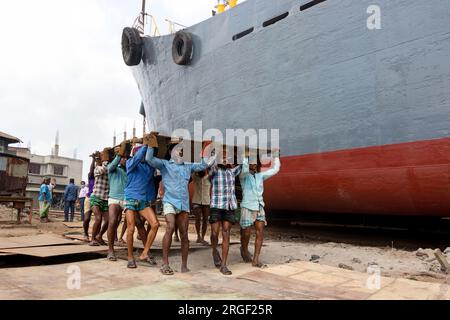 Dhaka, Dhaka, Bangladesch. 9. Aug. 2023. Eine Gruppe von Gepäckträgern trägt eine schwere Stahlplatte von 250 kg auf einer Werft am Ufer des Buriganga in Keraniganj, nahe Dhaka, Bangladesch. Dutzende von Werften, die 30,96 Hektar an der Küste von Buriganga belegen, sind seit 50 Jahren in Betrieb. Es wird hauptsächlich zur Reparatur und Reparatur alter Schiffe und zum Bau neuer Schiffe verwendet. Die Arbeit auf dem Werftplatz funktioniert ohne Helme, Gesichtsmasken oder Sicherheitsschuhe. Sie arbeiten den ganzen Tag lang hart, erhalten aber trotzdem Mindestlöhne. Mit einer zunehmenden Anzahl von Bestellungen sowohl von lokalen als auch von globalen Käufern, ist der Schiffbauer Stockfoto