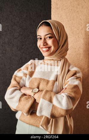 Minimales Porträt einer lächelnden Araberin, die an einer zweifarbigen Wand steht und selbstbewusst in die Kamera schaut Stockfoto