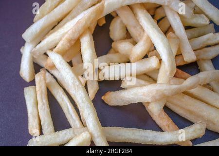 Pommes frites: Nahaufnahme mit frisch zubereiteten und perfekt goldenen Pommes frites vor dunklem Hintergrund. Der Fokus liegt auf einem fachmännischen Ansatz Stockfoto