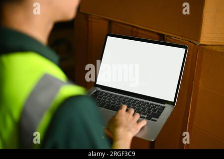 Gekürzte Aufnahme eines Lagerarbeiters, der zwischen Regalen steht, mit Pappkartons und Laptop Stockfoto