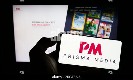 Person, die ein Mobiltelefon mit dem Logo des französischen Verlagsunternehmens Prisma Media auf dem Bildschirm vor der Unternehmenswebseite hält. Konzentrieren Sie sich auf das Display des Telefons. Stockfoto