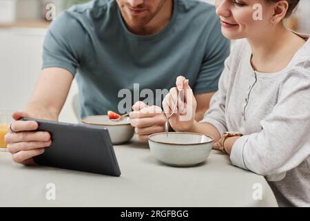 Nahaufnahme eines jungen Paares, das ein digitales Tablet benutzt, während es in der Küche frühstückt, in Kopierräumen Stockfoto