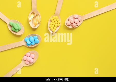 Vitamine auf gelbem Hintergrund, Draufsicht. Pillen verschiedener Farben in Holzlöffeln, flach liegend. Arzneimittel, Vitamine und Nahrungsergänzungsmittel Stockfoto