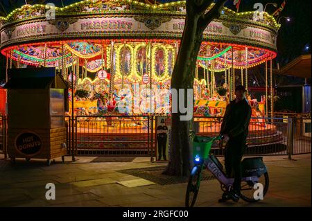 LONDON - 22. April 2023: Nachtzauber: Das hell beleuchtete Karussell schmückt Southbank, Londons lebendige Nacht, und ein E-Bike trägt zur dynamischen Szene bei Stockfoto