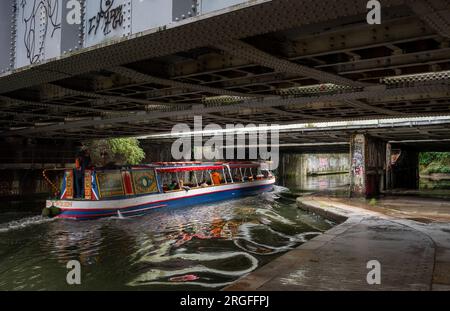 London, Großbritannien: Ein Touristenboot auf dem Regent's Canal in London mit Bewegungsunschärfe. Das Boot fährt unter einer Straßenbrücke in der Nähe von St. John's Wood hindurch. Stockfoto