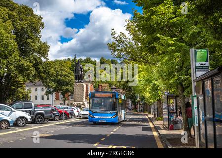 Ein blauer Eindeckbus fährt an Bushaltestellen vorbei, neben der riesigen Statue von König Alfred dem Großen am Broadway in Winchester, Hampshire, Großbritannien. Stockfoto