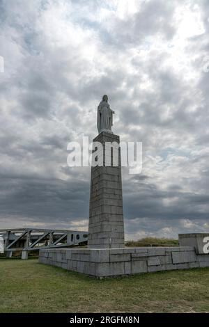 Arromanches-les-Bains, Frankreich - 07 21 2023: Denkmal für Veteranen, die Statue der Jungfrau Maria und Metallbrücke unter bewölkter Sonne Stockfoto