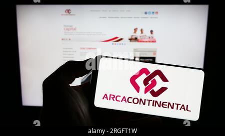 Person, die ein Mobiltelefon mit dem Logo des Unternehmens Arca Continental SAB de CV auf dem Bildschirm vor der geschäftlichen Webseite hält. Konzentrieren Sie sich auf das Display des Telefons. Stockfoto