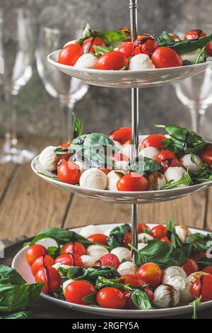 Klassischer italienischer Salat Insalata Caprese mit Kirschtomaten, Mini-Mozarella-Perlen, Basilikumblättern und Balsamglasur, serviert auf einem Kuchenstand, vertikal Stockfoto