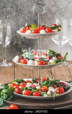 Klassischer italienischer Salat Insalata Caprese mit Kirschtomaten, Mini-Mozarella-Perlen, Basilikumblättern und Balsamglasur, serviert auf einem Kuchenstand, vertikal Stockfoto