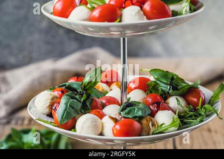 Klassischer italienischer Salat Insalata Caprese mit Kirschtomaten, Mini-Mozarella-Perlen, Basilikumblättern und Balsamic-Glasur, serviert auf einem Kuchenstand, aus nächster Nähe Stockfoto