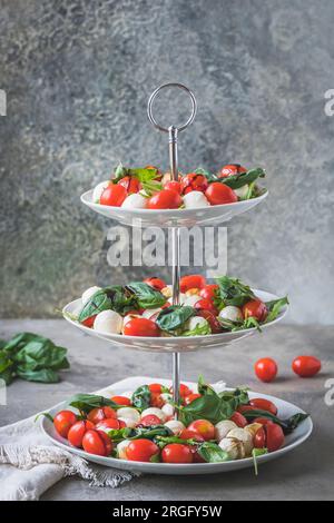 Klassischer italienischer Salat Insalata Caprese mit Kirschtomaten, Mini-Mozarella-Perlen, Basilikumblättern und Balsamglasur, serviert auf einem Kuchenstand, vertikal Stockfoto