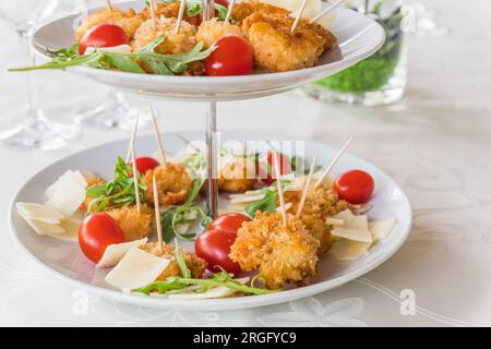 Gebratene panierte Garnelen mit Rucolasalat auf einem Porzellankuchenstand auf einem weißen, elegant gedeckten Tisch Stockfoto