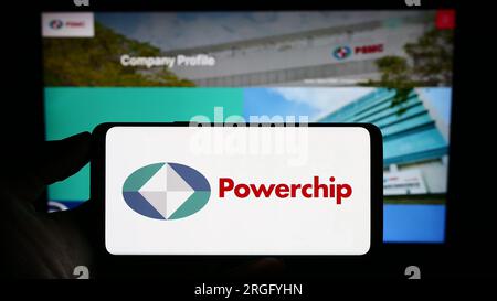 Person, die ein Mobiltelefon mit dem Logo der Powerchip Technology Corporation (PSMC) auf dem Bildschirm vor der Webseite hält. Konzentrieren Sie sich auf das Display des Telefons. Stockfoto