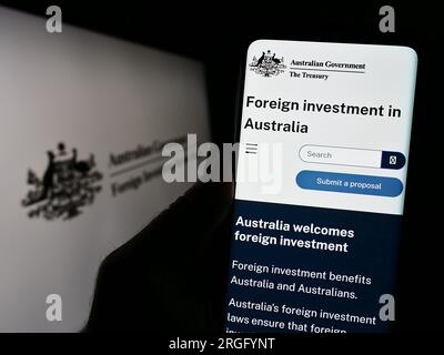 Person, die ein Mobiltelefon mit einer Webseite des Australian Foreign Investment Review Board (FIRB) auf dem Bildschirm mit Logo besitzt. Konzentrieren Sie sich auf die Mitte des Telefondisplays. Stockfoto