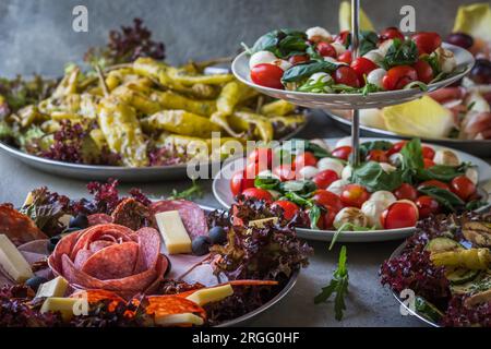 Italienisches Vorspeisenbuffet mit gegrilltem Gemüse, gegrillten Peperoni, Schinken, Salami, Salatcaprese auf grauem Hintergrund Stockfoto