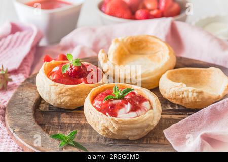 Hausgemachte Croissant-Brötchen gefüllt mit Sahne und Erdbeerpüree auf einem Holztablett Stockfoto