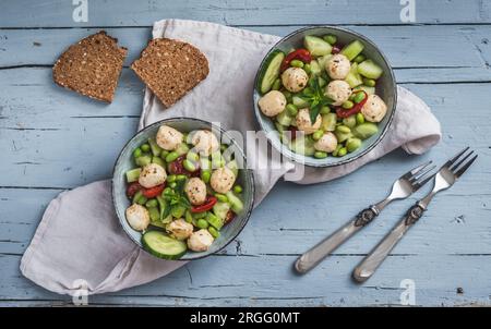 Sommersalat mit Gurke, Mini-Tomaten, Mini-Mozzarella und Sojabohnen auf hellblauem Holzhintergrund, Draufsicht Stockfoto