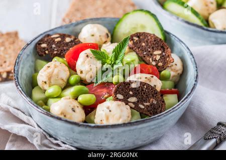 Sommersalat mit Gurke, Mini-Tomaten, Mini-Mozzarella und Sojabohnen auf weißem Holzhintergrund Stockfoto