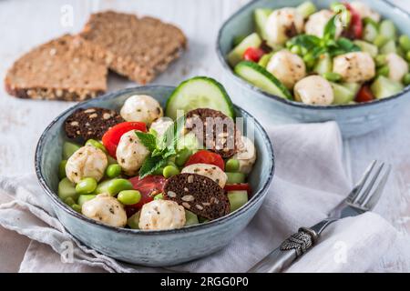 Sommersalat mit Gurke, Mini-Tomaten, Mini-Mozzarella und Sojabohnen auf weißem Holzhintergrund Stockfoto