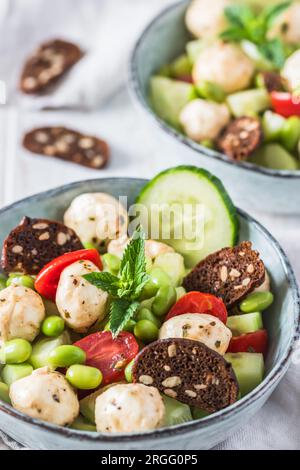 Sommersalat mit Gurke, Mini-Tomaten, Mini-Mozzarella und Sojabohnen auf weißem Holzhintergrund, vertikal Stockfoto