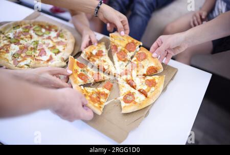 Auf dem Tisch sind zwei offene Boxen Pizza, jeder der bestehenden Menschen nimmt Stück. Stockfoto