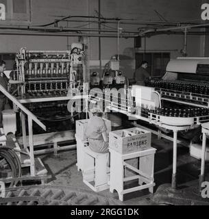 1950er, historisch, das Innere einer Getränkeabfüllanlage, Malta, zeigt einen Mann und eine Frau, die an der Abfüllanlage arbeiten und das Förderband überwachen. Eine Holzkiste neben der weiblichen Arbeiterin trägt den Namen Farsons, die erste Brauerei auf der Insel, die 1928 gegründet wurde. Stockfoto