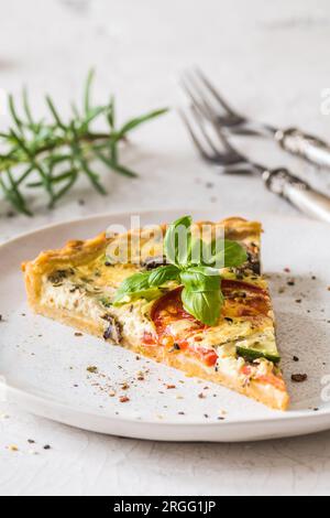 Stück Gemüsetorte mit Pilzen, Tomaten und Zucchini auf weißem Hintergrund, vertikal Stockfoto