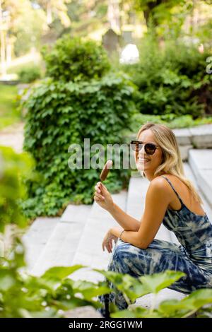 Hübsche junge Frau, die auf der Treppe sitzt und Eis am Stiel isst Stockfoto