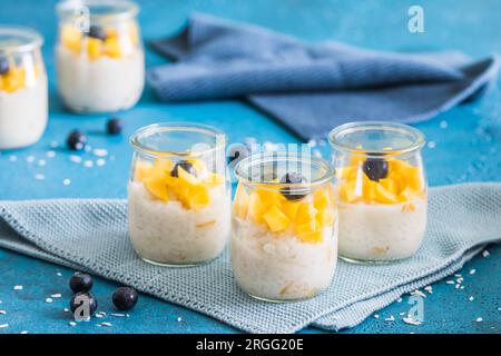 Kokosreis-Pudding mit Mango in Dessertgläsern auf blauem Hintergrund Stockfoto