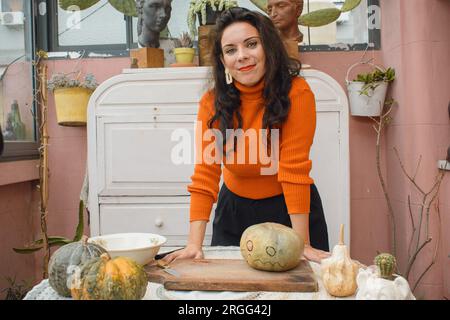 Porträt einer erwachsenen, kaukasischen Künstlerin, die Kürbis für Halloween dekoriert, Inhalte für ihre sozialen Netzwerke macht, sie steht mit ihren Händen auf Stockfoto