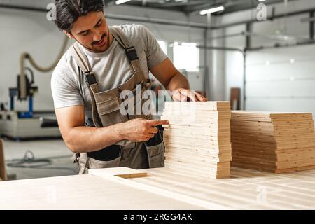 Junger Zimmermann sucht und wählt Holzbohle in einer Werkstatt in einer Holzfabrik Stockfoto