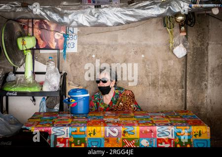 Eine alte thailändische Dame sitzt in einem thailändischen Café oder Restaurant im Freien in der Sanam Khli Alley, Bangkok, Thailand. Stockfoto