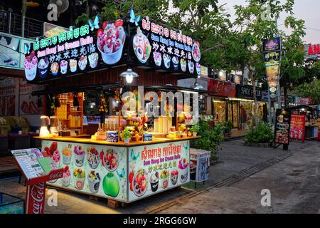 Siem Reap, Kambodscha, 22. Dezember 2022. Urbane Erfrischungen: Ein Straßenwagen mit Obst und Getränken, umgeben von lebhaften urbanen Schildern. Stockfoto